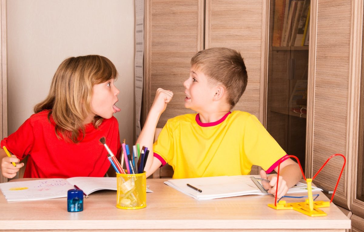 Children quarreling. Sister teasing brother while doing homework together. ©
